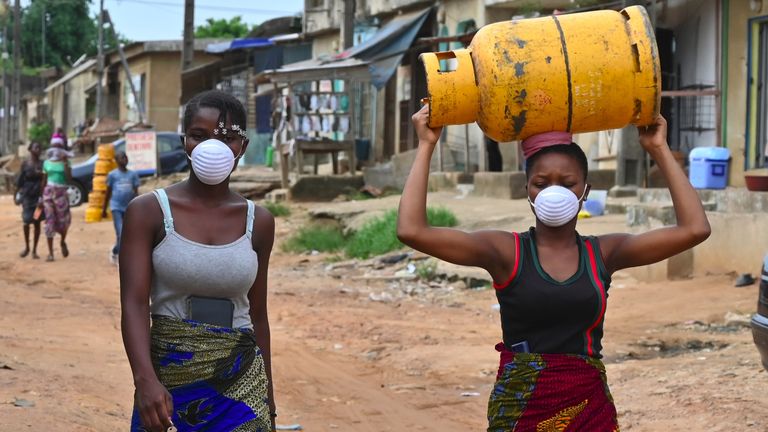 Une femme porte une bouteille de gaz sur la tête tout en portant un masque 