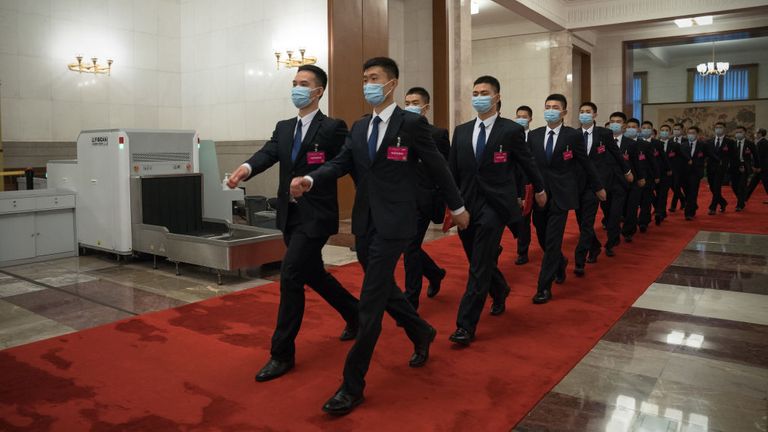 Des agents de sécurité portant des masques faciaux marchent à l'intérieur de la Grande Salle du Peuple
