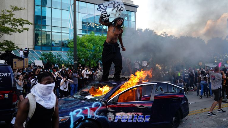 Un homme se tient au sommet d'une voiture de police en flammes lors d'une manifestation contre la mort de George Floyd à Minneapolis alors qu'il était en garde à vue devant le CNN Center le 29 mai 2020 à Atlanta, en Géorgie. (Photo par Elijah Nouvelage / Getty Images)