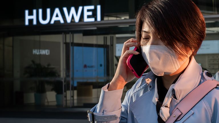 Une femme portant un masque facial comme mesure préventive contre le coronavirus COVID-19 parle sur son smartphone à l'extérieur d'un centre commercial devant une boutique Huawei (arrière) à Pékin le 1er avril 2020.