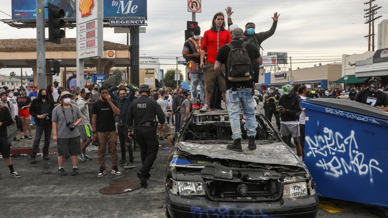 Des manifestants se tiennent au sommet d'une voiture de police incendiée à Los Angeles