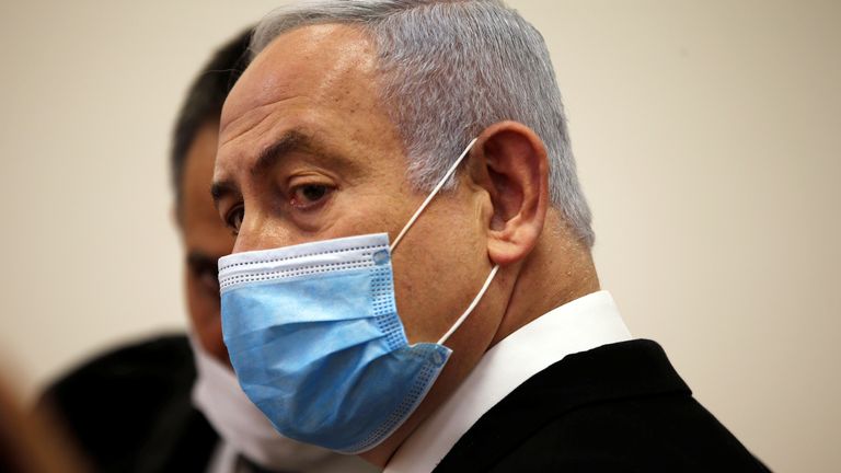 Le Premier ministre israélien Benjamin Netanyahu, portant un masque facial, regarde debout à l'intérieur de la salle d'audience alors que son procès pour corruption s'ouvre devant le tribunal de district de Jérusalem