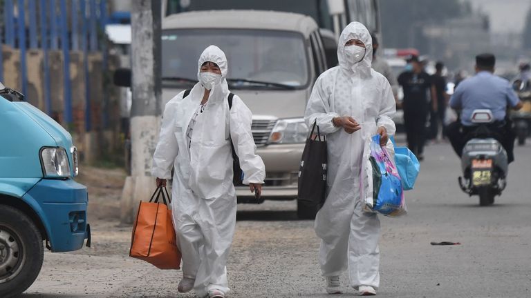 Deux femmes portent des combinaisons de protection lorsqu'elles marchent dans une rue près du marché fermé de Xinfadi à Pékin