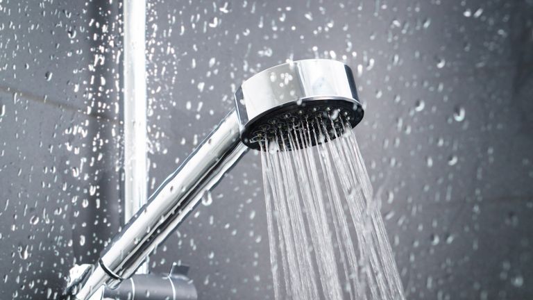 Douche fraîche derrière la fenêtre en verre humide avec des éclaboussures de gouttes d'eau.  L'eau qui coule de la pomme de douche et du robinet dans la salle de bains moderne.