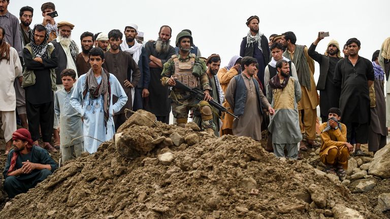 Un personnel de sécurité (C) monte la garde parmi les villageois qui se rassemblent alors que les sauveteurs recherchent des corps dans la province de Parwan