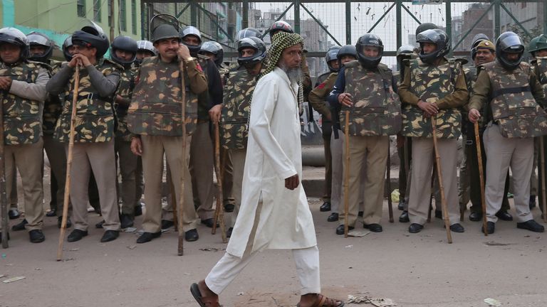 Un musulman passe devant des policiers qui montent la garde à côté d'une mosquée dans une zone touchée par les émeutes à la suite d'affrontements entre des personnes manifestant pour et contre une nouvelle loi sur la citoyenneté à New Delhi