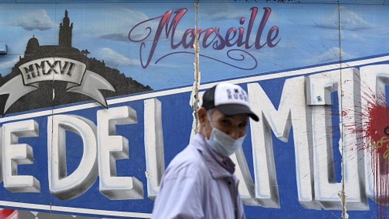 Un homme portant un masque facial marche devant un graffiti à Marseille