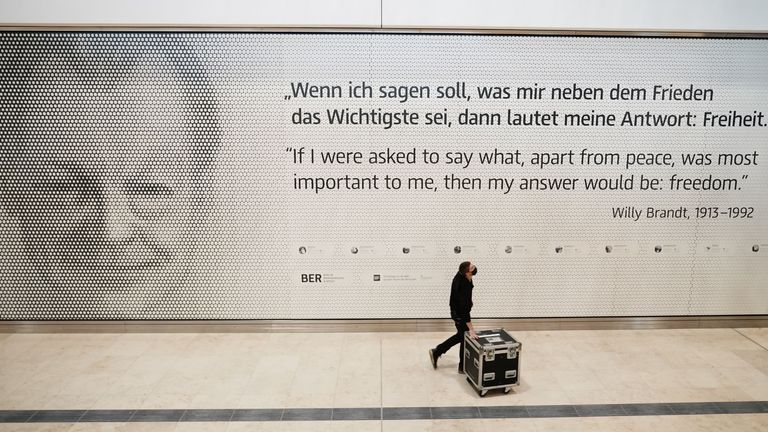 Un employé entre dans le terminal 1 de l'aéroport international Berlin-Brandebourg Willy-Brandt (BER) devant une photo de l'ancien chancelier allemand Willy Brandt à Schoenefeld, près de Berlin, le 27 octobre 2020. - Neuf ans de retard et dépassant le budget, le nouvel aéroport international de la région de Berlin ouvrira enfin le 31 octobre 2020 - au milieu d'une pandémie mondiale qui a paralysé les voyages aériens.  (Photo par Michael Kappeler / POOL / AFP) (Photo par MICHAEL KAPPELER / POOL / AFP via Getty Images)
