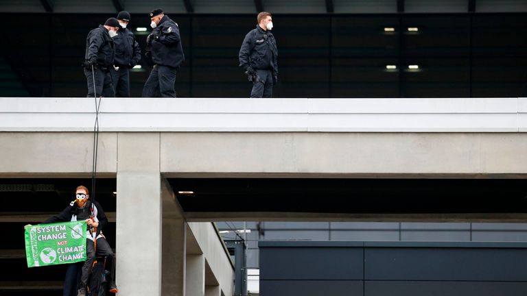 Un activiste climatique habillé en pingouin tenant une banderole est détenu par des policiers alors qu'il est suspendu au toit du terminal principal de l'aéroport de Berlin 