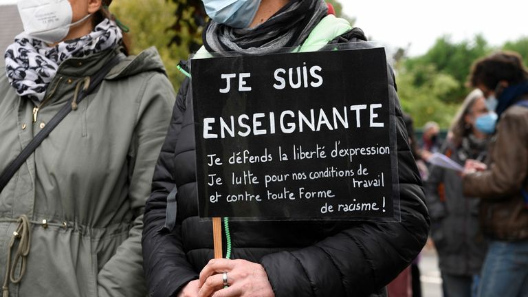 Un enseignant se tient debout avec une pancarte indiquant `` Je suis enseignant, je défends la liberté d'expression, je me bats pour nos conditions de travail et contre toute sorte de racisme '' près de l'entrée d'un collège à Conflans-Sainte-Honorine, à 30kms au nord-ouest de Paris, le 17 octobre 2020, après la décapitation d'un enseignant par un agresseur abattu par des policiers
