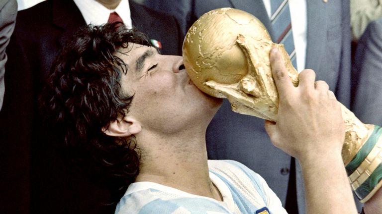 Le capitaine de l'équipe star du football argentin Diego Maradona embrasse la Coupe du monde de football remportée par son équipe après une victoire 3-2 sur l'Allemagne de l'Ouest le 29 juin 1986 au stade Azteca de Mexico, regardé par le président mexicain Miguel de La Madrid (L) et l'Ouest Le chancelier allemand Helmut Kohl.  (Photo par STAFF / AFP) (Photo par STAFF / AFP via Getty Images)