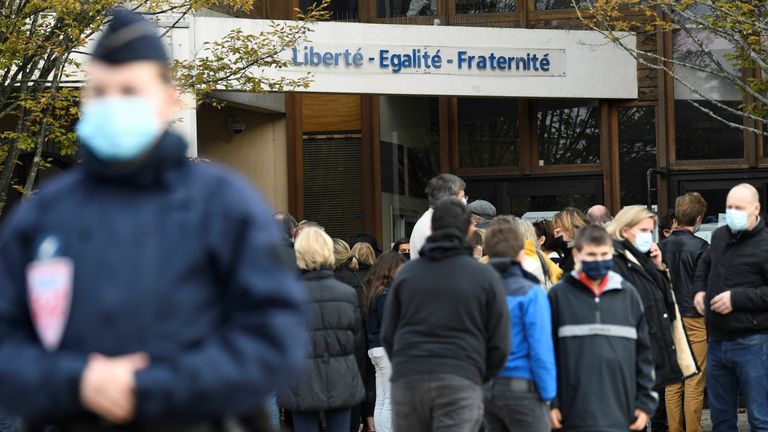 Les intervenants d'urgence (SAMU) passent devant des policiers du CRS debout devant un collège à Conflans-Sainte-Honorine, à 30 km au nord-ouest de Paris, le 17 octobre 2020, alors que des fleurs sont affichées après qu'un enseignant a été décapité par un assaillant qui a été abattu mort par des policiers