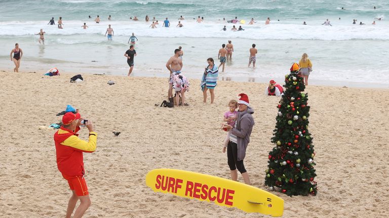 Une personne dans un bonnet de Noel pose pour une photo avec un enfant près d'un arbre de Noël le jour de Noël à Bondi Beach à Sydney, Australie, le 25 décembre 2020. REUTERS / Loren Elliott