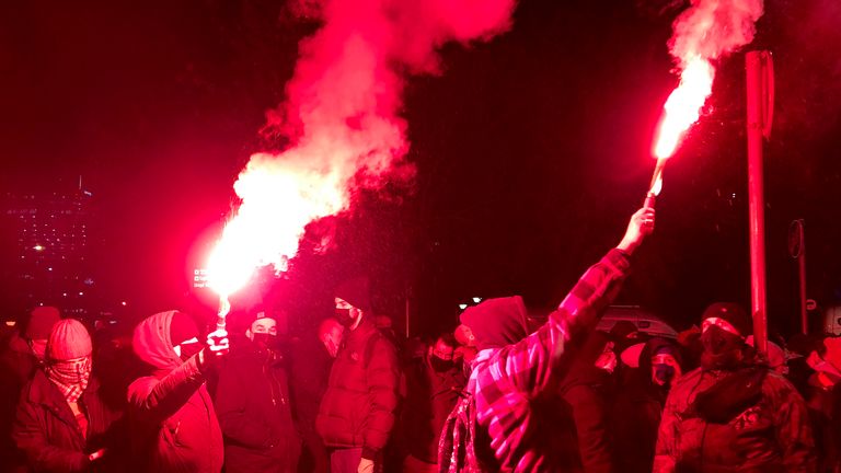 Les gens allument des fusées éclairantes alors qu'ils marchent près du siège du parti au pouvoir à Varsovie, en Pologne.  Pic: AP