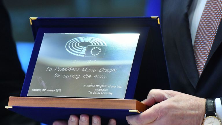 Le président de la Banque centrale européenne, Mario Draghi, reçoit un cadeau des membres du Parlement européen avant de s'adresser à la commission des affaires économiques et monétaires du Parlement européen à Bruxelles le 28 janvier 2019 (Photo par EMMANUEL DUNAND / AFP) (Crédit photo doit se lire EMMANUEL DUNAND / AFP / Getty Images)