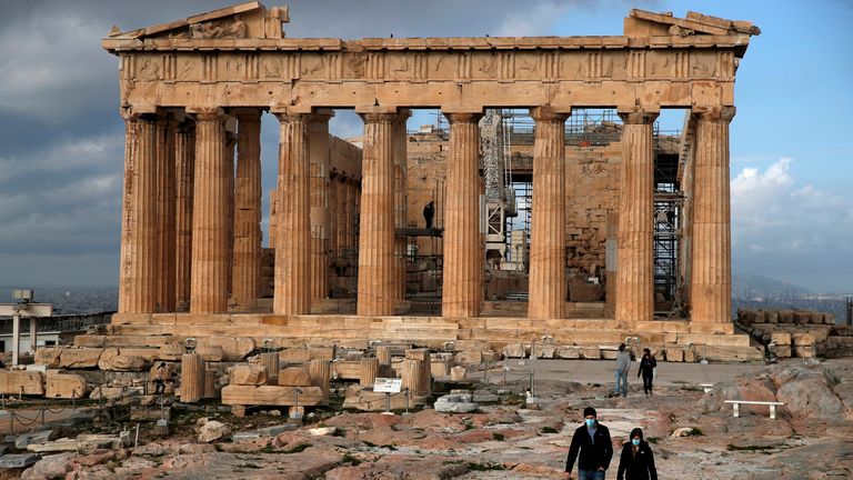 Les premiers visiteurs portant des masques faciaux pour se protéger contre la propagation du coronavirus, marchent au sommet de la colline de l'Acropole, alors que le temple du Parthénon est vu en arrière-plan à Athènes, le lundi 22 mars 2021. Le gouvernement grec a rouvert l'Acropole et d'autres sites antiques dans tout le pays après quatre mois alors qu'il se prépare à redémarrer la saison touristique à la mi-mai.  (Photo AP / Thanassis Stavrakis)