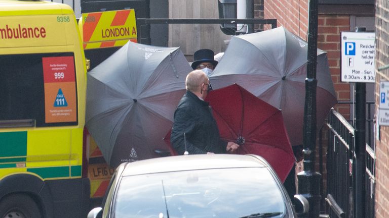Le personnel protégeait un patient entrant dans une ambulance avec des parapluies