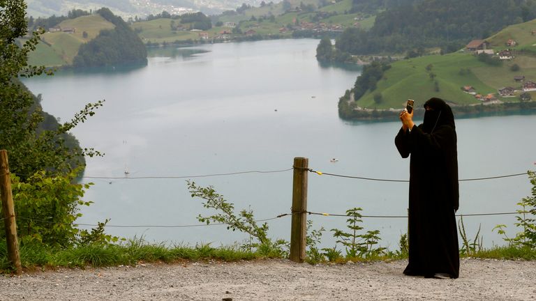 Une femme portant un niqab prend une photo d'un belvédère au-dessus du lac Lungenersee à la route du col du Bruenigpass, Suisse 